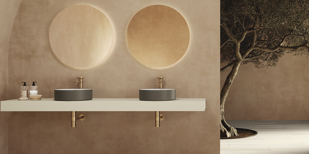 Baño moderno con lavabos dobles sobre encimera flotante blanca, espejos redondos retroiluminados y diseño natural con tonos tierra.