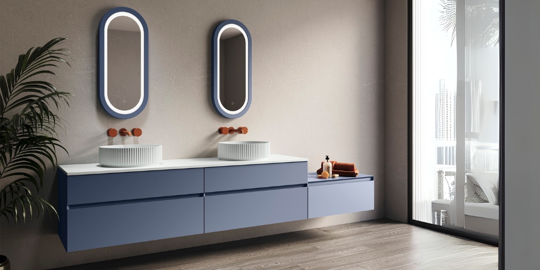Mueble de baño flotante azul con lavabos sobre encimera, grifería en cobre y espejos LED ovalados.