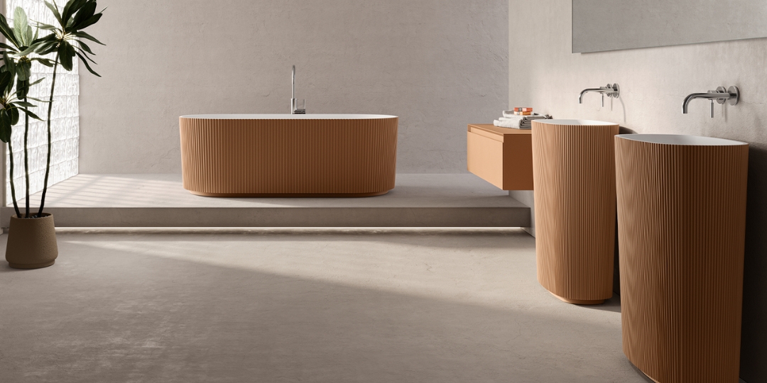 Baño moderno con bañera y lavabos de pie color terracota, muebles suspendidos y luz natural.