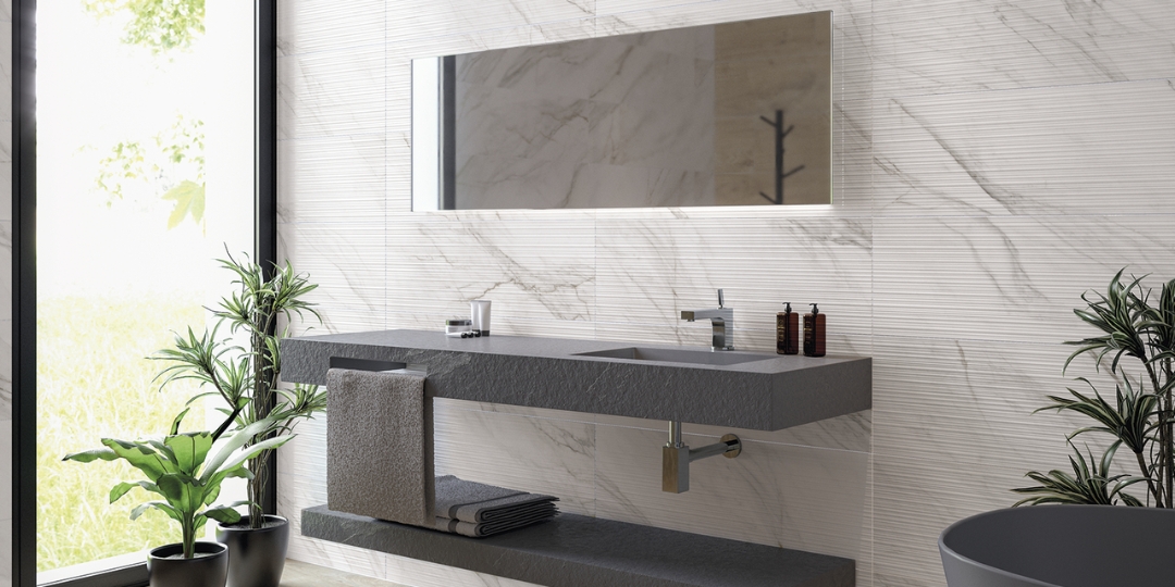 Baño con lavabo solid surface de piedra gris suspendido, pared cerámica imitación mármol y espejo retroiluminado